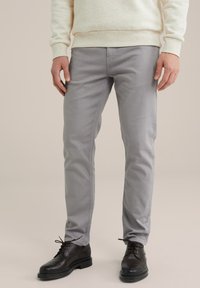 Gray chinos with a slim fit design, made from a smooth cotton blend. Worn with black leather shoes and a light cream sweater.