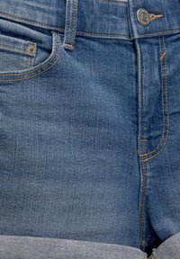 Short en denim bleu avec couture orange, bouton en métal et poche avant avec petite poche à monnaie visible.