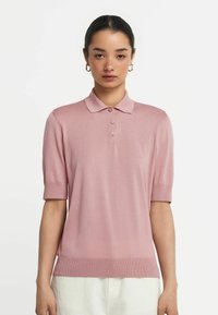 Rosa polo skjorta med korta ärmar, ribbat avslut och tre-knappars knappslå. Tillverkad av ett glatt tyg, med en klassisk krage.