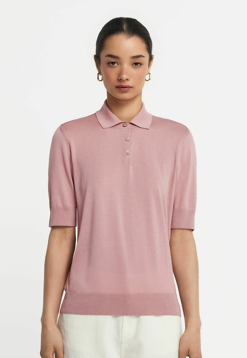 Rosa polo skjorta med korta ärmar, ribbat avslut och tre-knappars knappslå. Tillverkad av ett glatt tyg, med en klassisk krage.