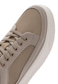 Sneaker beige con materiali in rete e canvas, punta rotonda, suola piatta in gomma bianca e occhielli tono su tono. Presenta dettagli di cuciture texture.