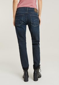 Dunkelblaue Denim-Jeans mit mittelhohem Bund, fünf Taschen, dezenten Nähten und einem braunen Leder-Logo-Patch am hinteren Bund.