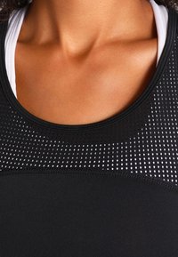 Zwarte atletische tanktop met een geprofileerd mesh paneel met kleine witte stippen bij de halslijn. Gladde stof en een aansluitend ontwerp.