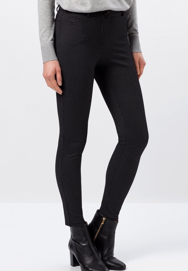 Pantalones negros ajustados con un patrón de pata de gallo texturizado, silueta ajustada y cintura de altura media, combinados con botas tobilleras.