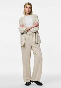 Ensemble en lin composé d'une veste à ouvrir et d'un pantalon à cordon de serrage dans une douce couleur beige. Des chaussures noires au design plat complètent le look.