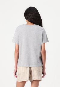 Gray cotton t-shirt with a relaxed fit, short sleeves, and a crew neckline, seen from the back. Paired with beige striped shorts.