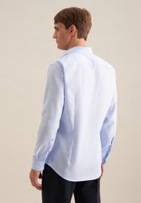 Camicia azzurro chiaro a maniche lunghe in tessuto liscio, con colletto a punta, polsini abbottonati e orlo dritto con spacchi laterali per una maggiore libertà di movimento.