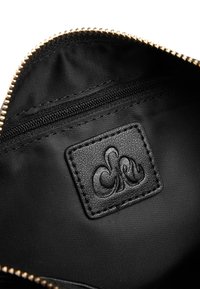 Interno di una borsa in tessuto nero con un patch in pelle testurizzata, zip dorata e una piccola tasca con zip su un rivestimento liscio.