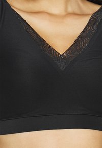 Black bralette with a V-neck design featuring a lace trim. Smooth texture with a fitted waistband. No padding or underwire visible.