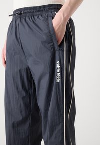 Marine blauwe trainingsbroek van lichtgewicht stof, met zijzakken, een tailleband met trekkoord en witte accenten aan de zijkanten met logo-print.