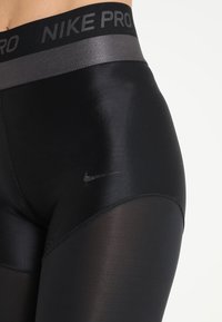 Leggings negros Nike Pro con una textura lisa y brillante, una cintura elástica gris y un pequeño logo discreto en el lateral.