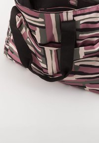Tote bag met abstract patroon in roze, beige en donkergroen; beschikt over zwarte stoffen handvatten en een ritsluiting. Geweven oppervlak met zakken.