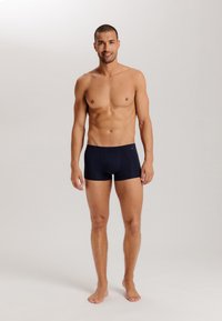 Mörkblå boxershorts i en åtsittande design, tillverkade av ett mjukt tyg med en bekväm midja. Modellen står utan överdel och barfota.