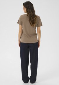 T-shirt marron à manches courtes avec un col ras du cou, associé à un pantalon ample bleu marine foncé, présentant une texture lisse et légère.
