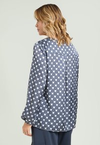 Langærmet bluse i let stof med geometrisk mønster i blå og hvid. Ryggen har en diskret lægedetalje.