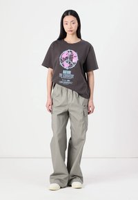 Grå grafisk T-shirt med et globusdesign og tekst, parret med lysegrå cargobukser. Outfitet har en afslappet pasform og bløde teksturer.