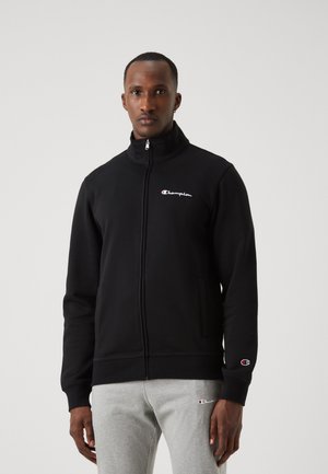 Sudadera con cremallera negra, hecha de tejido suave, que cuenta con un alto cuello, bolsillos frontales y un pequeño logo de Champion en el pecho y en la manga.