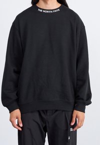 Černá mikina vyrobená z měkké tkaniny, s širokým výstřihem a žebrovanými manžetami. Na límci je bíle vytištěno logo "THE NORTH FACE".