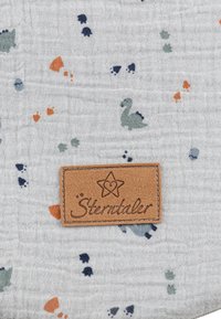 Helles, graues, strukturiertes Gewebe mit bunten Mustern von Fußabdrücken und einem Dinosaurierdesign. Enthält ein braunes Lederetikett mit geprägtem Branding.