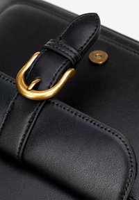 Detail černé kožené tašky s zlatou kovovou sponou, prošitými detaily a hladkým povrchem. Design obsahuje zabezpečený klapku.