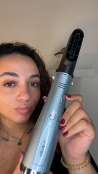 Silver handheld hair dryer with a black nozzle, features buttons and ventilation slots, smooth surface, and round metal base.