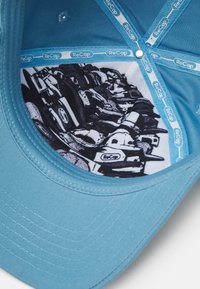 Turkis baseballcap med et mykt tekstilbelegg. Inni har den et svart og hvitt design som viser ulike kjøretøy, merket med "ReCap."