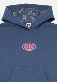 Sweatshirt azul com bolso frontal, logótipo rosa "Roxy Since 90" no peito e forro com padrão floral dentro do capuz.