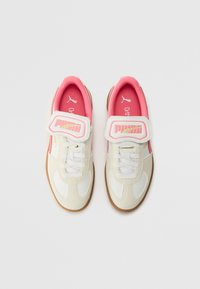 Baskets blanches et beige clair avec des accents roses, dotées d'une sangle velcro, d'un laçage et d'une semelle en caoutchouc texturée.