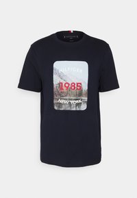 Námořnická modrá bavlněná tričko s potiskem přední strany zobrazením krajinné scény a nápisem "HILFIGER 1985 NEW YORK" v bílém a červeném písmu.