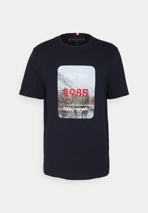 Námořnická modrá bavlněná tričko s potiskem přední strany zobrazením krajinné scény a nápisem "HILFIGER 1985 NEW YORK" v bílém a červeném písmu.