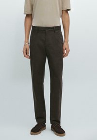 Donkerbruine katoenen broeken met een rechte pasvorm, met een sluiting met een knoop aan de voorkant en zijzakken. Draag ze met een beige shirt met korte mouwen en bruine schoenen.