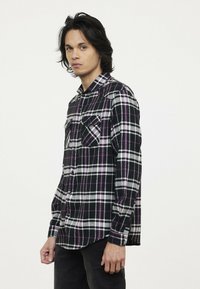 Zwart-wit geruite shirt met paarse accenten, voorzien van twee borstzakken, een knoopsluiting kraag en lange mouwen. Zachte stoftextuur.