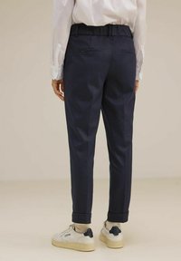 Pantaloni tapered blu navy con finitura testurizzata, dotati di vita elasticizzata e orli arrotolati, abbinati a sneaker bianche.