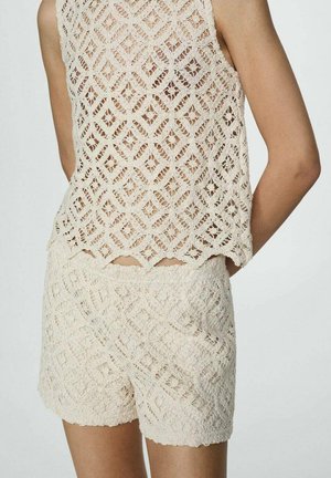 Beige haaktop en shorts set met een geometrisch kantpatroon, textuurafwerking en geschulpte randen. De achterkant is open.