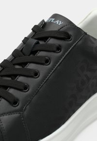 Baskets en cuir noir avec lacets noirs, motif répétitif subtil "REPLAY" sur les côtés, et semelle blanche.