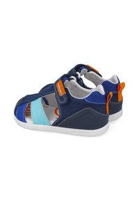 Sandalias azul marino con acentos en azul claro y naranja. Hechas de tela, con un diseño abierto, tira ajustable y suela de goma blanca.
