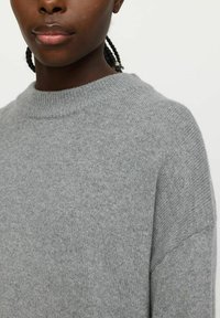 Hellgrauer, gestrickter Pullover mit Rundhalsausschnitt, weichem Material und lockerer Passform. Sichtbare Nahtdetails an den Schultern verleihen einen oversized Look.