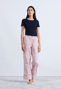 Marinblå t-shirt med kort ärm i kombination med lösa rosa byxor med knappfront och kontrasterande röd kant vid fållen. Mjuk bomullstextur.