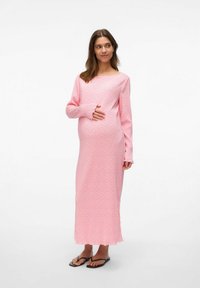 Zwangere jurk van zacht roze stof met een bloemenpatroon, lange mouwen, een bateauhals en een enkellange ontwerp. Gekocht met zwarte teenslippers.