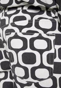 Närbild av svartvita byxor med ett djärvt, retro geometriskt mönster som visar sammanlänkade fyrkantiga former och synlig stygn på bakfickan.