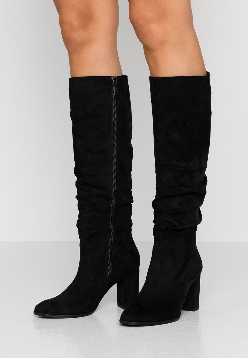 Black suede knee-high boots with a slouchy design, side zipper detail, and a block heel. Smooth texture and pointed toe.