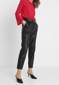 Rotes Langarmoberteil mit Glockenärmeln, hoch taillierte schwarze Lederhosen und schwarze spitze Slip-On-High-Heels. Einfaches, tailliertes Design.
