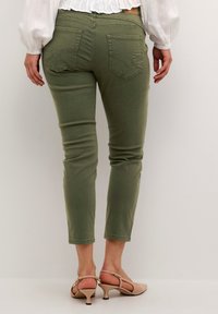 Pantaloni slim-fit de culoare verde măsliniu, cu design cu cinci buzunare, detalii cusute și mansete rulate deasupra gleznei, asortați cu pantofi cu toc bej.