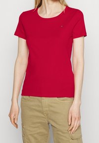 Rød bomulds T-shirt med korte ærmer og rund halsudskæring. Har et lille logo på den øverste venstre brystregion. Glat tekstur.