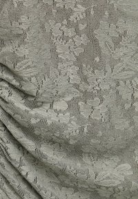 Tissu en dentelle gris clair avec des motifs floraux complexes et des plis doux montrant la texture et les détails.