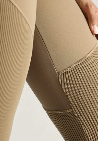 Bež legging aktivne odjeće s glatkom i rebrastom teksturom; ima dizajn u blok bojama s ravnim šavovima i prilagođenim oblikom.
