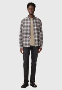 Gray plaid button-up shirt over a beige t-shirt, paired with dark jeans and black boots. Smooth fabric, relaxed fit, and subtle details.