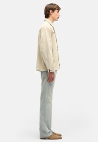 Beżowa kurtka ze sztruksu z kołnierzem, zapinana z przodu na guziki, w połączeniu z jasnymi dżinsami i beżowymi botkami do kostki. Subtelne kontrasty faktur.