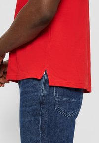 Chemise rouge à manches courtes avec une finition texturée, dotée d'ouvertures latérales au niveau de l'ourlet. Assortie à un jeans en denim bleu offrant une coupe classique.