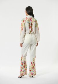 Floral-embroidered, lightweight white blouse with long sleeves paired with white trousers featuring vibrant floral hems and tailored fit.